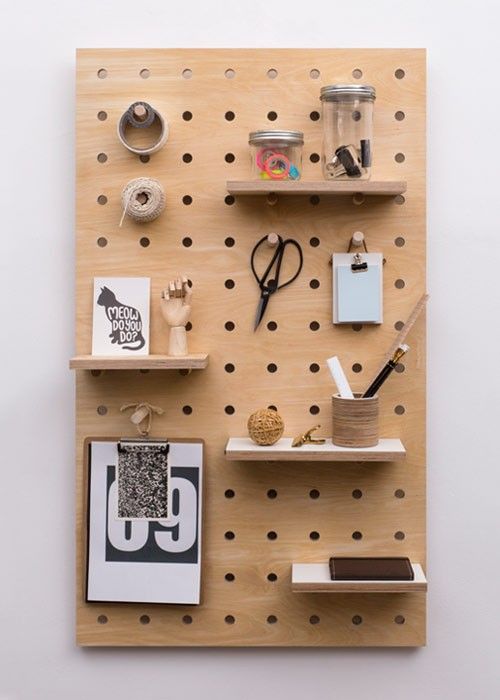 the image shows a peg board where the user has put up shelfes on pegs that stores jars, a poster, books and other office supplies.