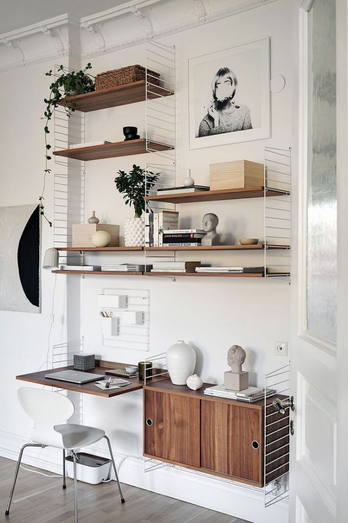 The picture shows string shelf with a foldable wall-mounted desk. On the desk, the user has a computer and notebooks.